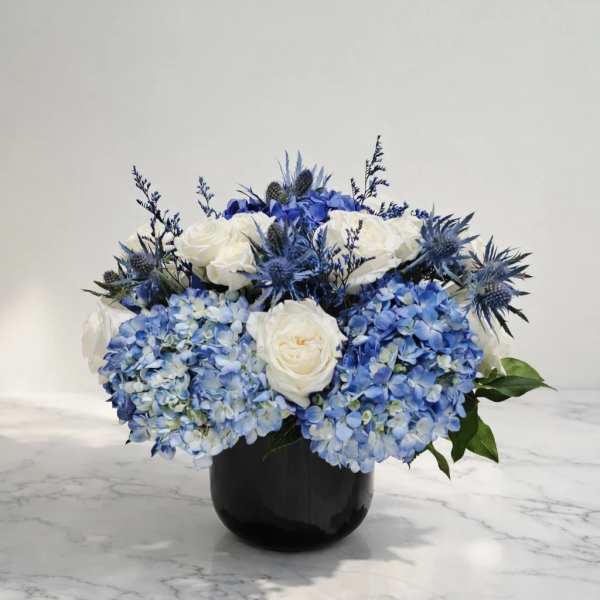 Blue hydrangeas and white roses arranged in a black vase
