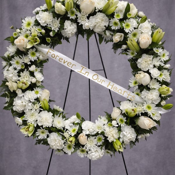 White funeral wreath with roses, lilies, and daisies on a stand