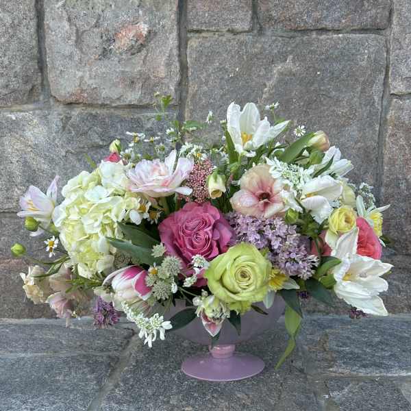 Low pink compote filled with pink roses, white tulips, hydrangeas, and mixed pastel blooms.