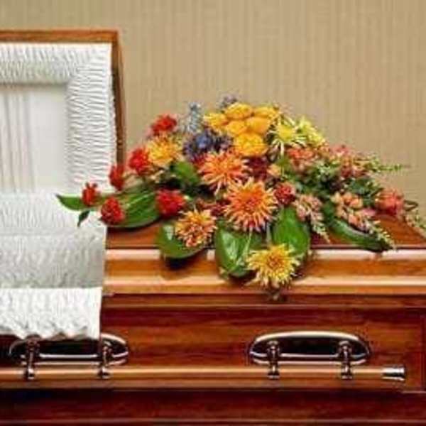 Colorful floral spray on a wooden casket beside a white quilted lining