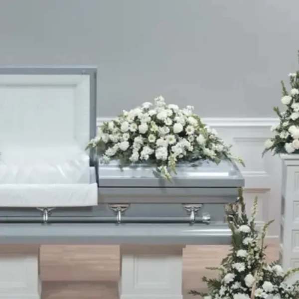 White floral casket spray on a silver casket in a funeral room