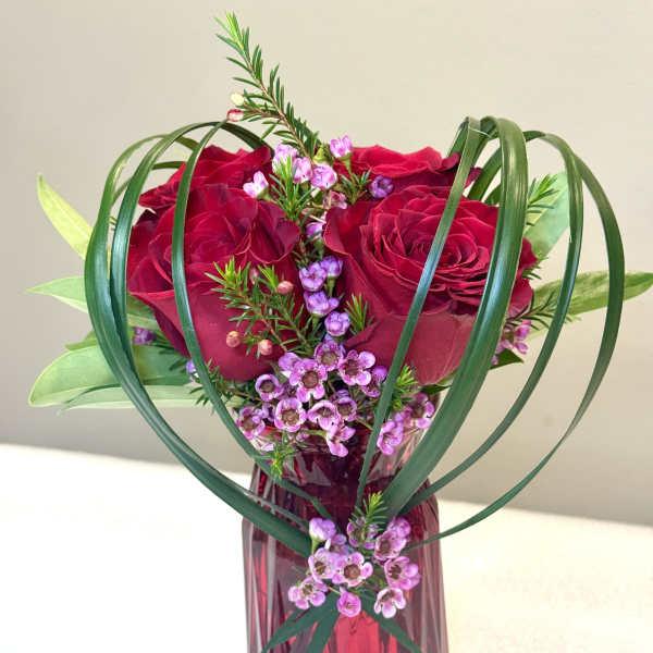 Red roses and pink filler flowers in a red glass vase