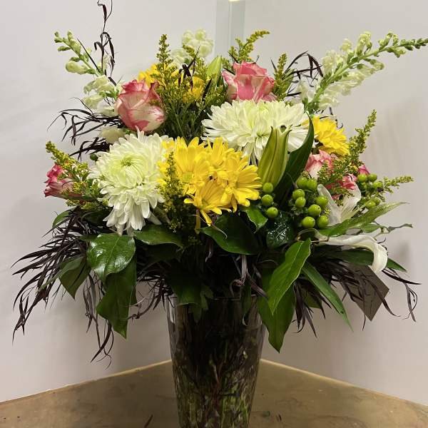 Mixed bouquet of white and yellow flowers in a tall glass vase