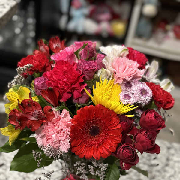 Mixed bouquet of red, pink, and yellow flowers in a glass vase with a red ribbon