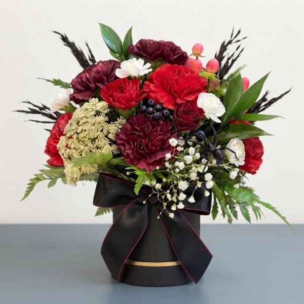 Red and white floral arrangement in a black hatbox with a ribbon