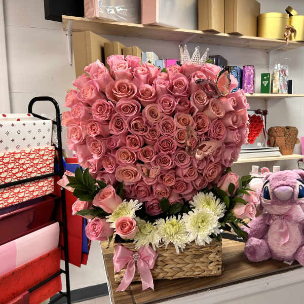 Heart-shaped pink rose arrangement in a basket with a plush purple toy beside it