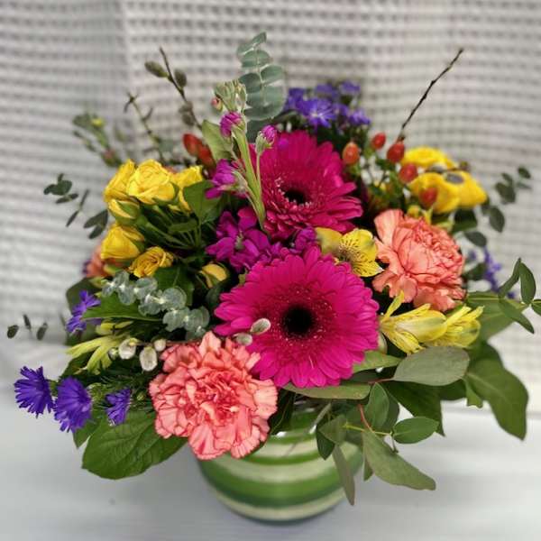 Bright mixed bouquet in a green-striped vase with pink, yellow, and purple flowers