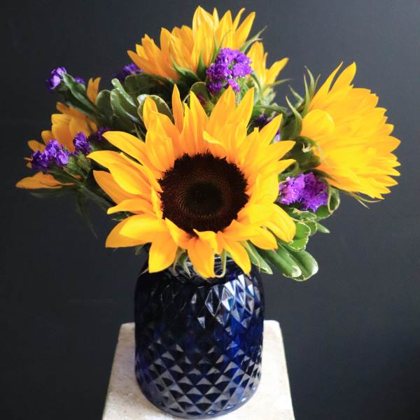 Sunflowers and purple filler flowers in a blue glass vase