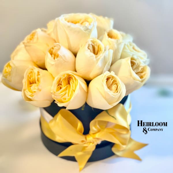 Cream roses arranged in a black hat box with yellow ribbon