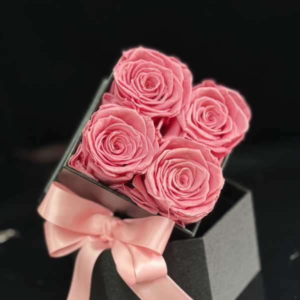 Four pink roses in a black gift box with a pink ribbon