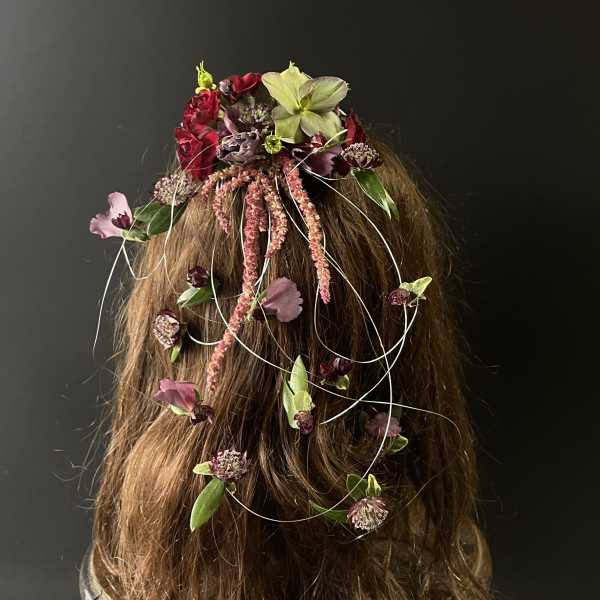 Floral hairpiece with red, pink, and green blooms on long hair