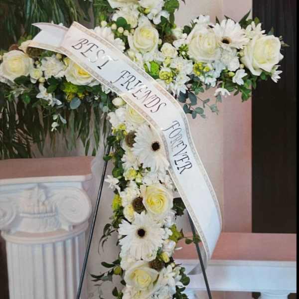 Standing floral cross of white roses and gerbera daisies with a Best Friends Forever ribbon.