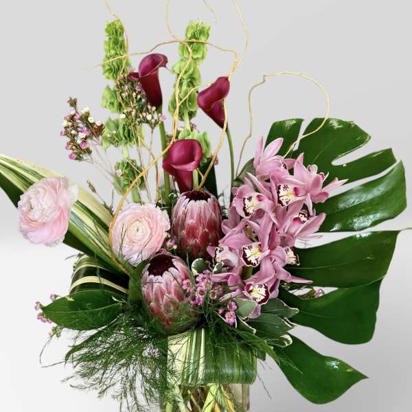 Pink orchids and calla lilies in a glass vase with tropical leaves
