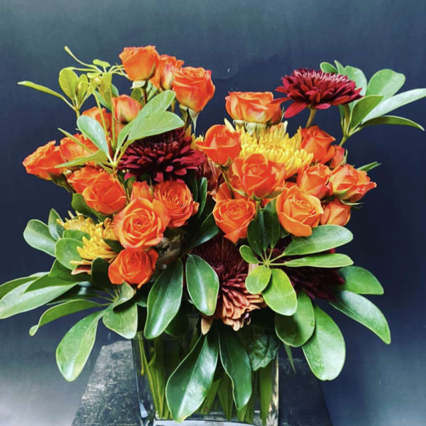 Orange roses and dark red chrysanthemums in a clear glass vase