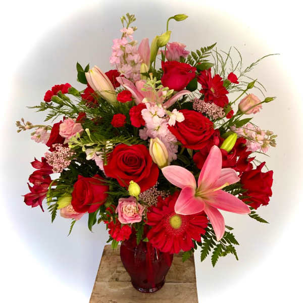 Red and pink roses, lilies, carnations, and gerbera daisies in a red glass vase