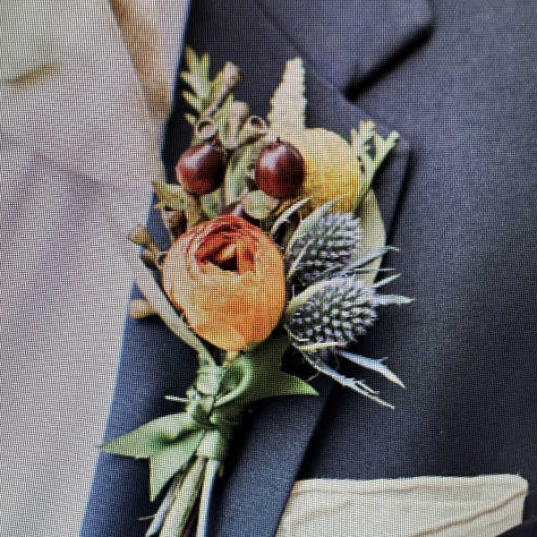 Orange and yellow boutonniere with berries and thistle on a dark suit lapel