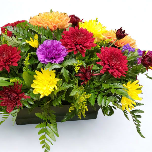 Low arrangement of red, yellow, orange, and purple blooms in a rectangular dark container