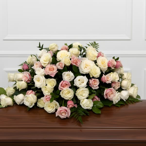 Casket spray of white and blush roses on a wooden casket