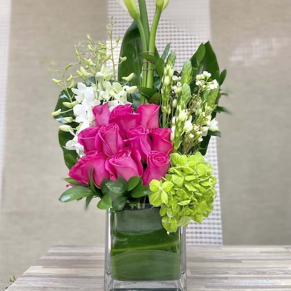 Tall modern arrangement with white calla lilies, hot pink roses, and green hydrangea in a glass cube vase