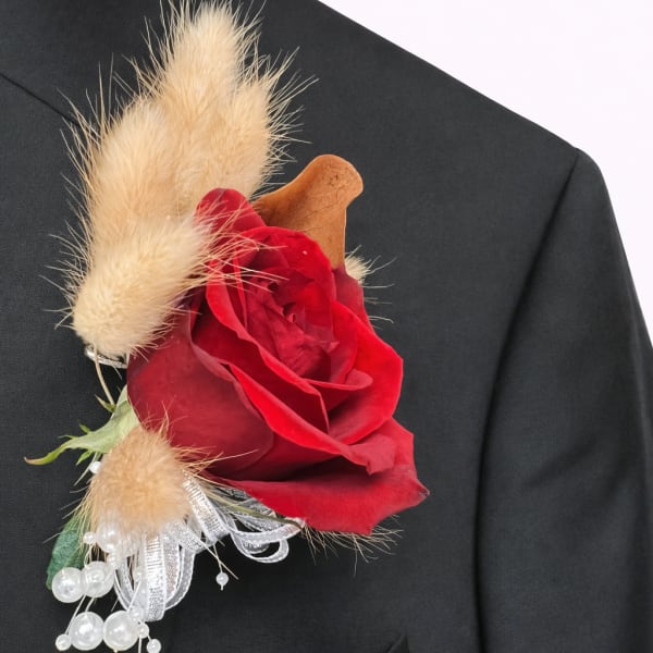 Red rose boutonniere with beige dried accents on a black suit lapel