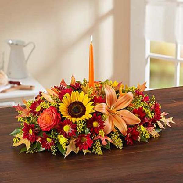 Low floral centerpiece with a sunflower, orange lily, and orange taper candle