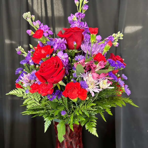 Red roses and purple mixed flowers in a red glass vase