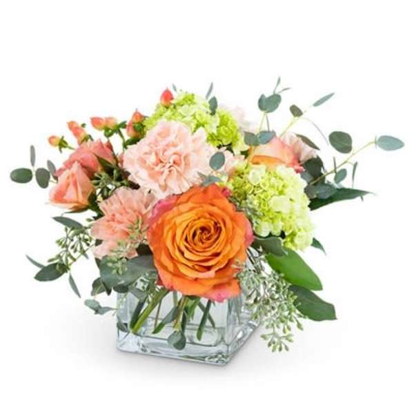Bouquet of orange and peach flowers in a square glass vase