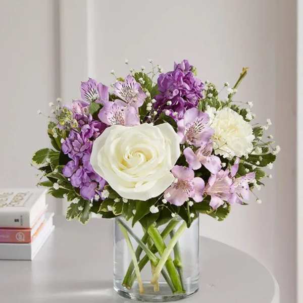 White rose and purple flowers in a clear glass vase
