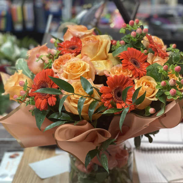 Orange roses and red gerbera daisies in a glass vase