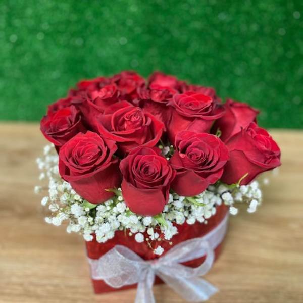 Short arrangement of red roses in a red box with white accent flowers and a white ribbon bow
