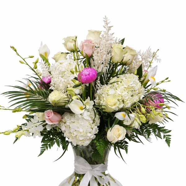 White and pink floral arrangement in a clear glass vase with a white ribbon
