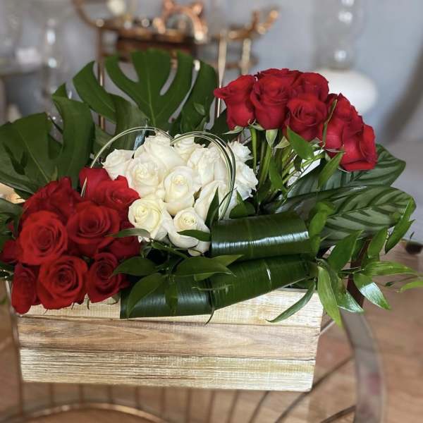Red and white roses arranged in a wooden box with large tropical leaves