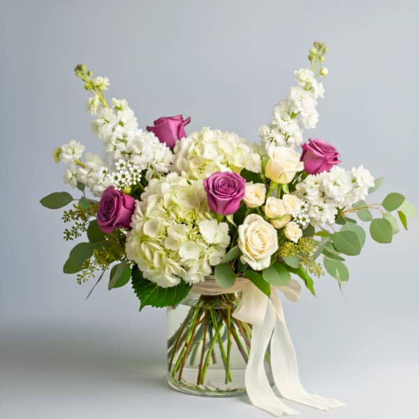 Bouquet of white hydrangeas and purple roses in a glass vase with a white ribbon