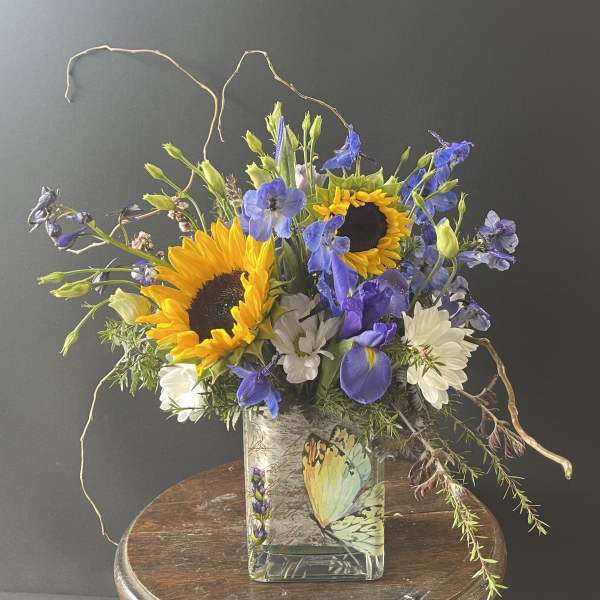 Bouquet of sunflowers, blue flowers, and white daisies in a glass vase