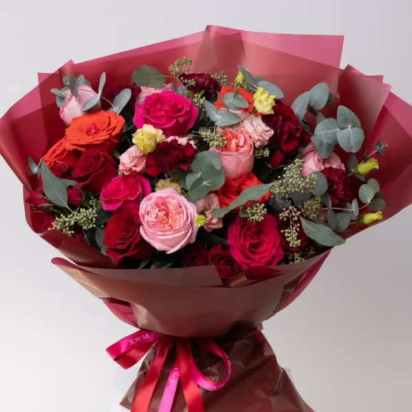 Bouquet of pink, red, and orange roses wrapped in burgundy paper