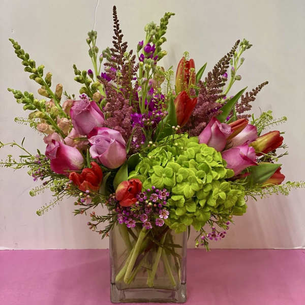 Pink roses and red tulips arranged with green hydrangea in a glass vase.