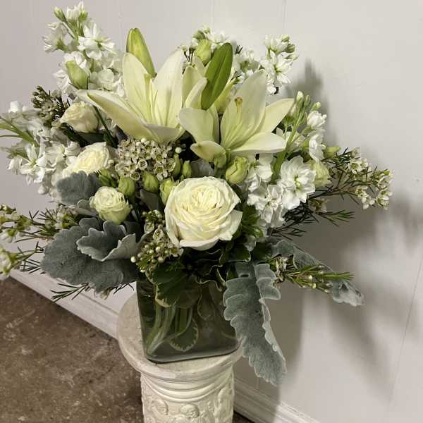 White lilies and roses arranged in a glass vase with silver foliage