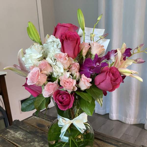 Pink roses and lilies arranged in a glass vase with a ribbon