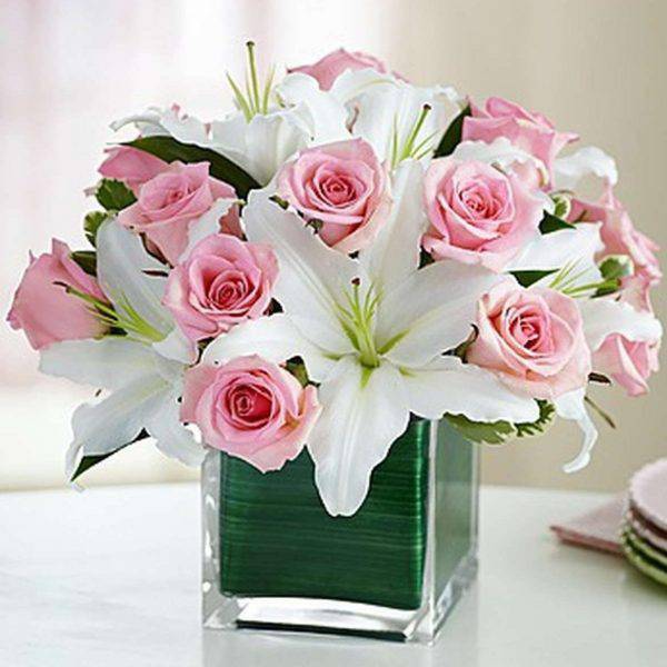Pink roses and white lilies arranged in a square glass vase
