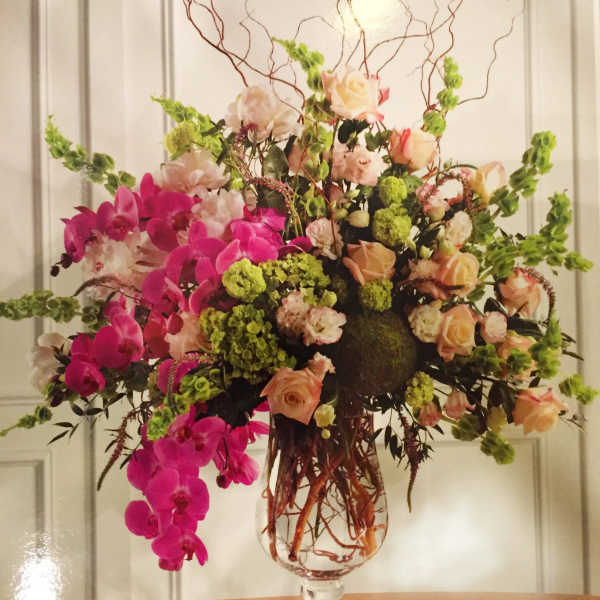 Large floral arrangement in a glass vase with pink orchids and peach roses