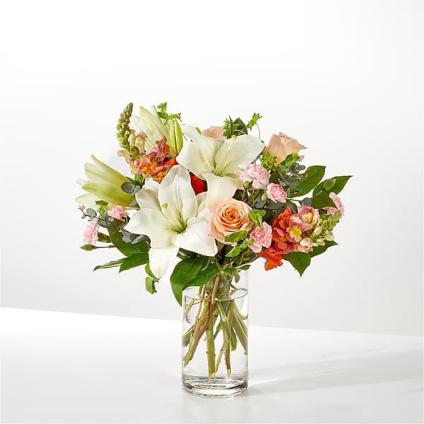 White lilies and peach roses in a clear glass vase