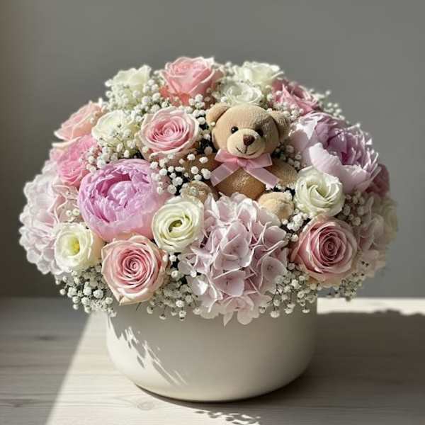 Pink and white flower arrangement with a teddy bear in a white bowl vase