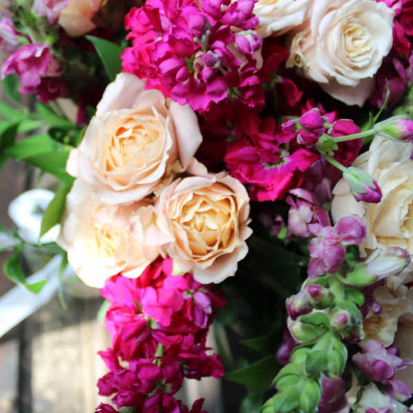Bouquet of peach roses and magenta flowers with white ribbon