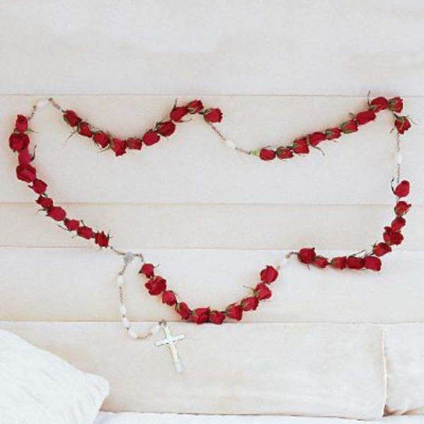 Red rose garlands draped across a white upholstered headboard with a small cross pendant