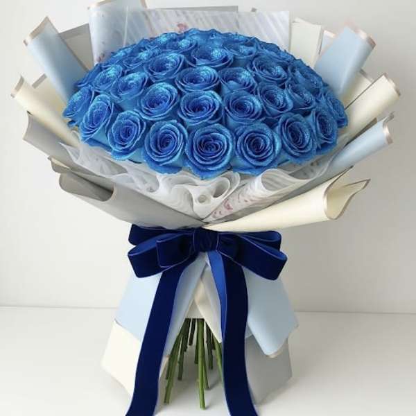 Bouquet of bright blue roses wrapped in pale paper with a navy ribbon
