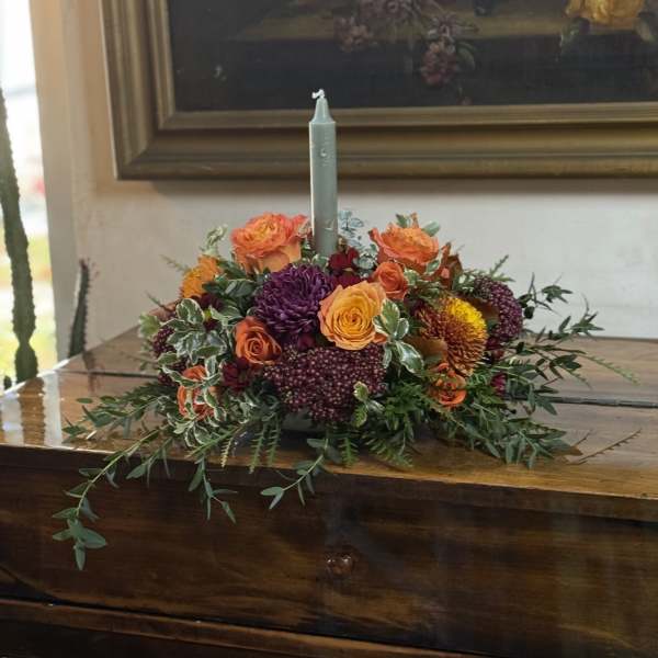 Low floral centerpiece with orange, yellow, and purple blooms around a candle