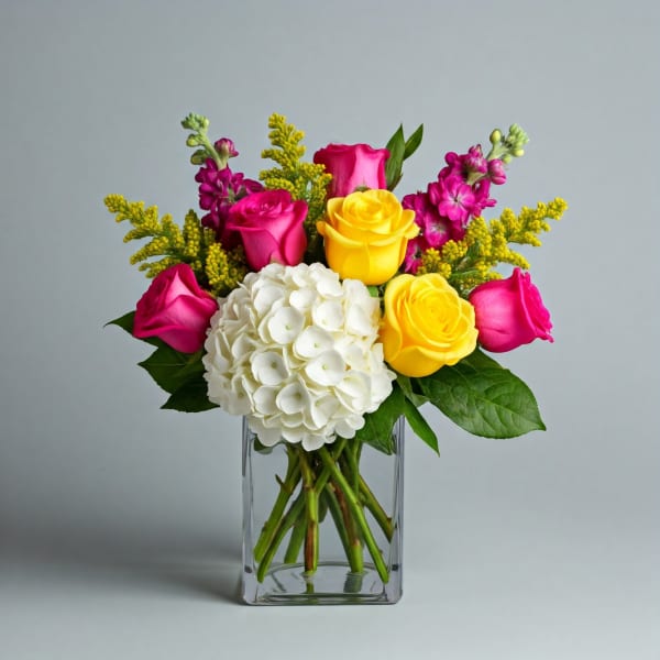 Bouquet of pink and yellow roses with white hydrangea in a clear glass vase