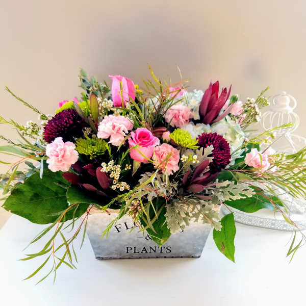 Mixed pink and burgundy floral arrangement in a metal planter box