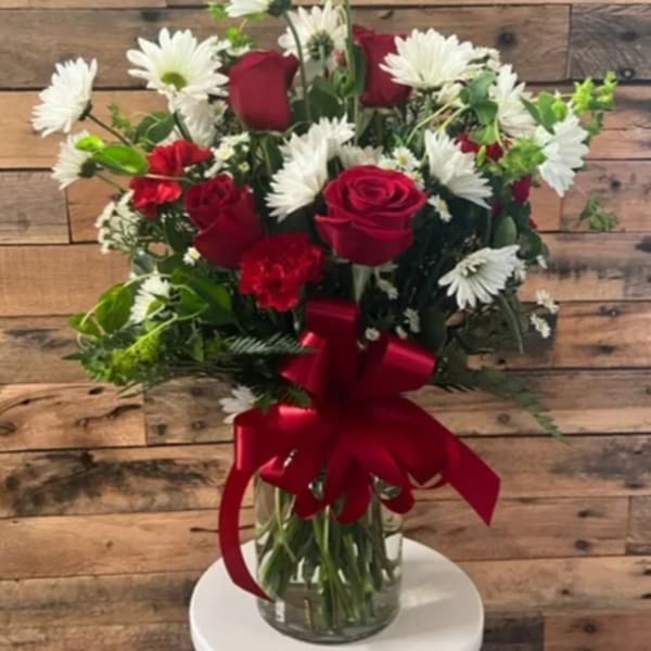 Red roses and white daisies in a glass vase with a red ribbon