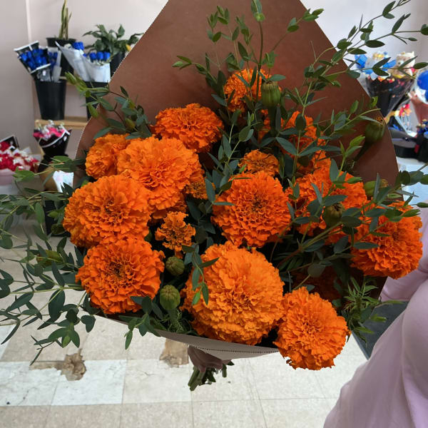 Bouquet of bright orange marigolds with greenery wrapped in brown paper